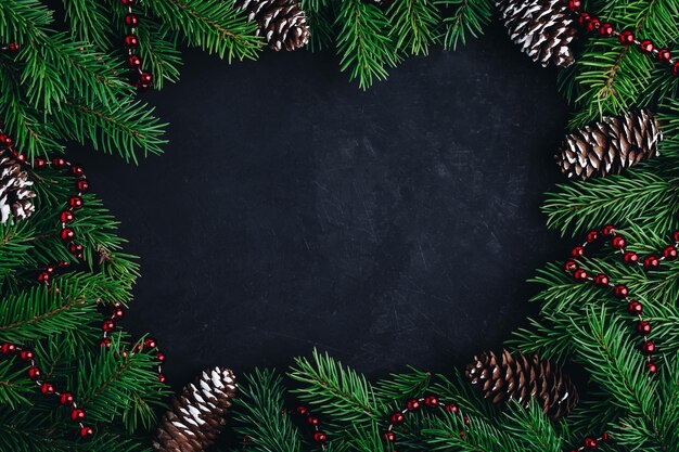 Weihnachtsfestlicher Layouthintergrund mit Fichtenzweigen, Kegeln und roter Girlande auf dunklem Hintergrund