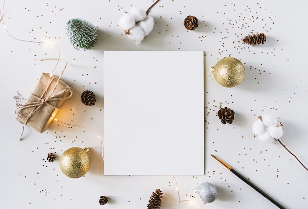 Weihnachtsfestschmuck und Grußkarte auf einer weißen rostigen Wand. Leeres Papier, Geschenk und Coton-Zweig mit glänzenden goldenen Kugeln.