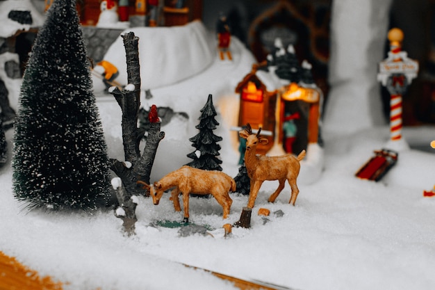 Weihnachtsfiguren von Hirschen und Weihnachtsbaum in der verschneiten Straße. Berühmte Lemax-Spielzeuge, Weihnachtswintergeschenke und -dekorationen.