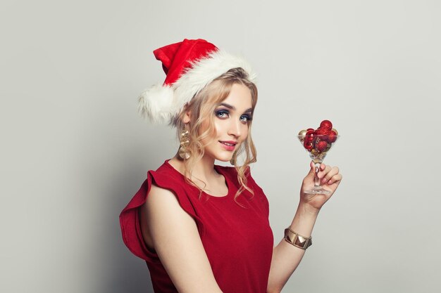 Weihnachtsfrau mit Weihnachtenmütze, die ein Glas Wein mit roter Weihnachtdekoration auf weißem Hintergrund hält