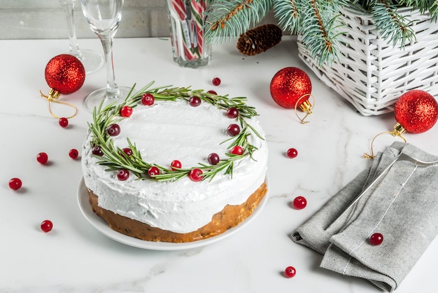 Weihnachtsfruchtkuchen oder -pudding, verziert mit Rosmarin und Moosbeere, mit Weihnachtsdekoration, auf weißer Marmortabelle