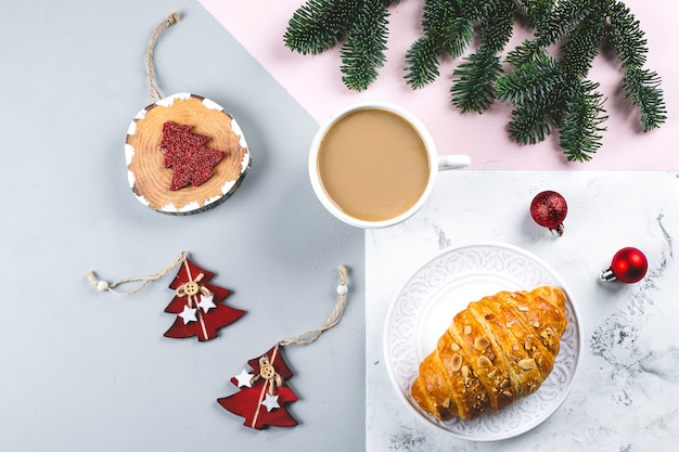 Weihnachtsfrühstück. Tasse Kaffee-, Hörnchen- und Feiertagsdekoration spielt, Baumtannenzweige auf dreifarbiger Tabelle. Hintergrund. Draufsicht, flach zu legen