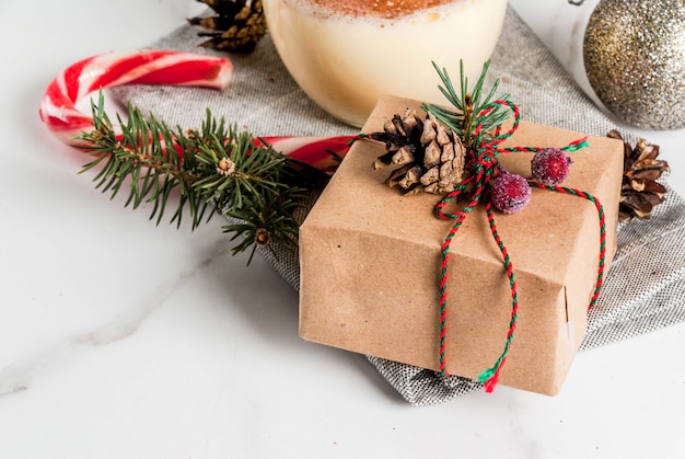 Weihnachtsgedeck mit traditionellem Wintereierpunsch, Weihnachtsgeschenk, Zuckerstange, Kiefernkegeln und Christbaumkugel