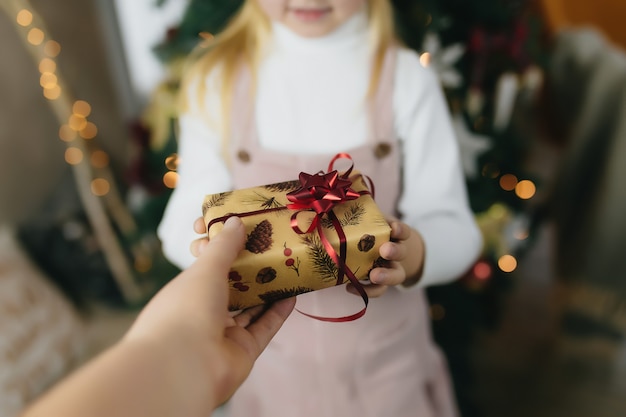 Weihnachtsgeschenk in Händen, Geschenk zu Hause, kleines Mädchen, das ein Weihnachtsgeschenk empfängt, Mädchen, das ein Weihnachtsgeschenk hält.