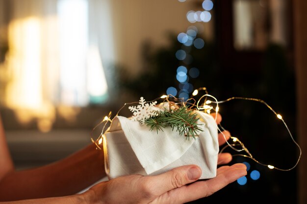 Weihnachtsgeschenk in Händen. Verpackung in umweltfreundlichen Materialien mit Lichtern