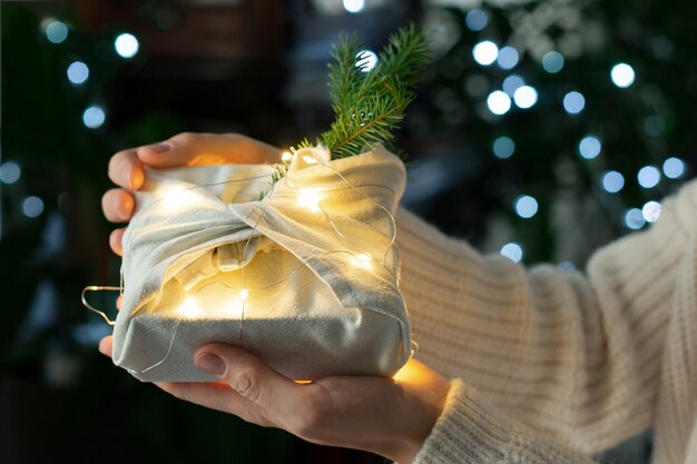 Weihnachtsgeschenk in Händen. Verpackung in umweltfreundlichen Materialien mit Lichtern