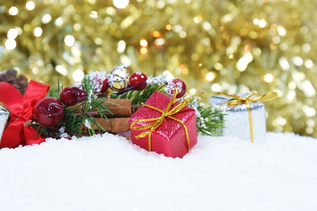 Weihnachtsgeschenk und -dekorationen im Schnee gegen ein Gold-bokeh beleuchtet Hintergrund