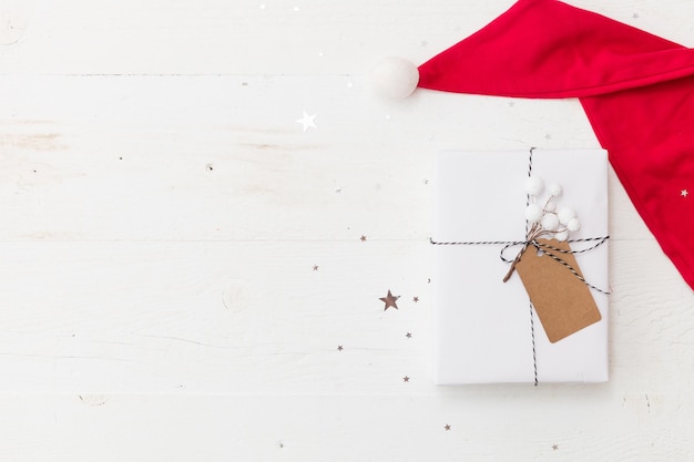 Weihnachtsgeschenk verpackt in weißem Geschenkpapier Weihnachtsschmuck in Santa's Hut auf hölzernen Hintergrund