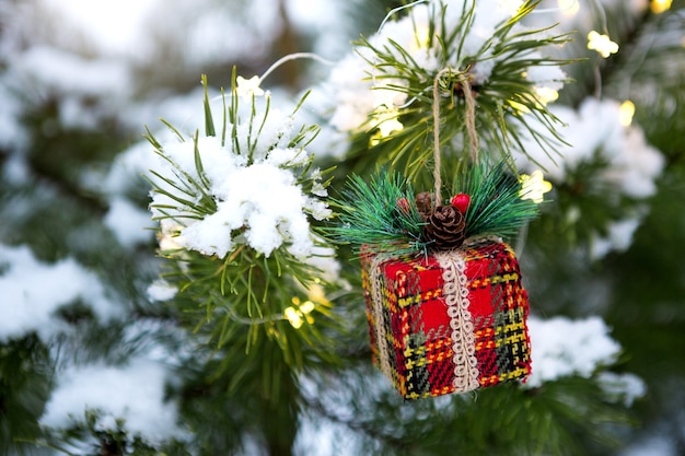 Weihnachtsgeschenkbox auf einem Zweig einer natürlichen Fichte mit Schnee bedeckt. Neues Jahr im Freien. Schneefall, Girlandenlichter, festliche Stimmung von Märchen und Magie, Straßendekoration. Platz kopieren