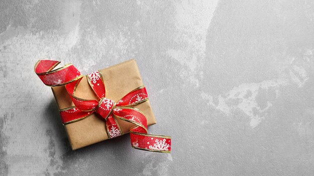 Weihnachtsgeschenkbox mit festlicher roter Banddekoration auf grauem Hintergrund, Draufsicht