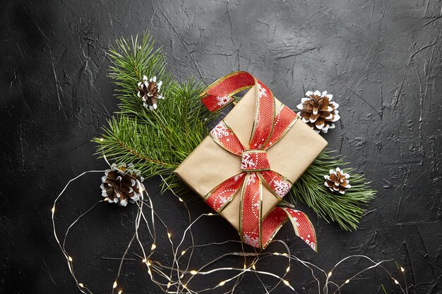 Weihnachtsgeschenkbox mit heller Girlande und Tannenzweigen mit Zapfen auf dunklem Hintergrund Draufsicht