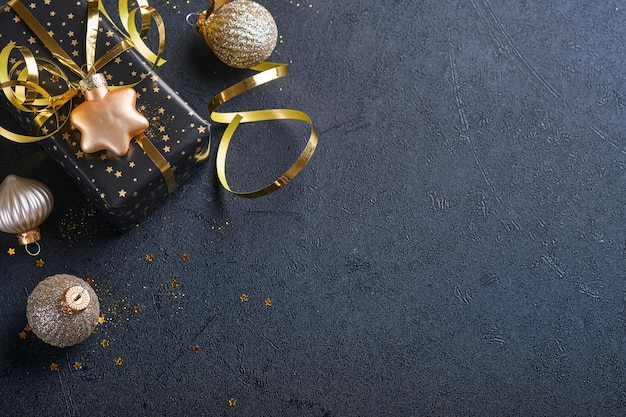 Weihnachtsgeschenkbox oder Geschenk mit Band, goldenem Konfetti und goldenen Kugeln auf schwarzem Hintergrund. Magische Weihnachtsgrußkarte. Weihnachtsdekoration. Grenzdesign. Attrappe, Lehrmodell, Simulation. Ansicht von oben.