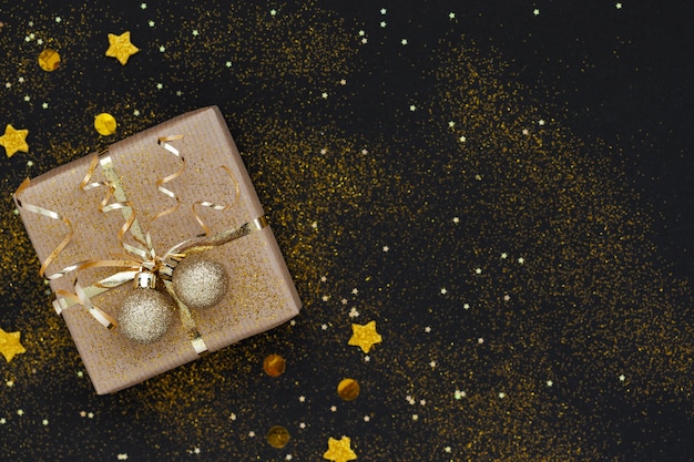 Weihnachtsgeschenkbox oder Geschenk verziert goldenes Band und zwei Kugeln auf schwarzem Hintergrund mit Funkeln.