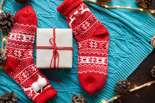 Weihnachtsgeschenkbox und rote Socken, ein blauer Strickpullover und eine Girlande mit Zapfen. Horizontale Ausrichtung