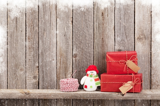 Weihnachtsgeschenkboxen und Schneemannspielzeug vor Holzwand. Ansicht mit Textfreiraum