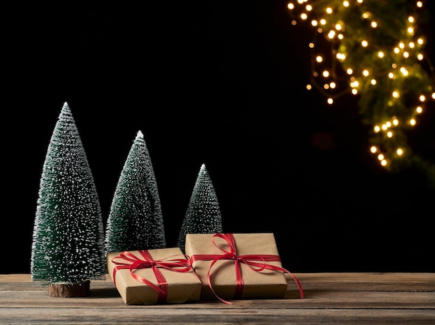 Weihnachtsgeschenkboxen und Tannenbaum auf Holztisch gegen unscharfe festliche Lichter, Platz für Text