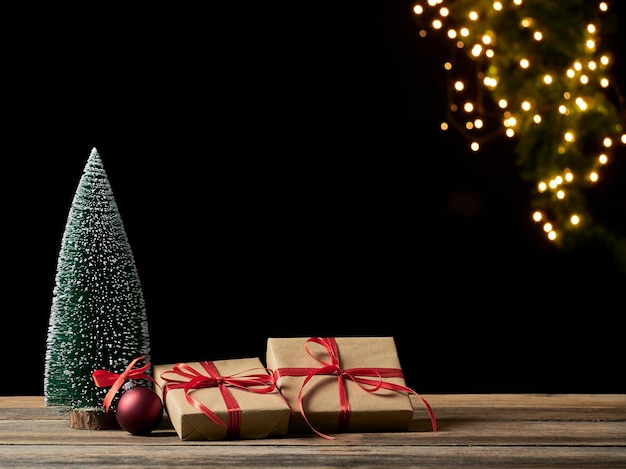 Weihnachtsgeschenkboxen und Tannenbaum auf Holztisch gegen unscharfe festliche Lichter, Platz für Text