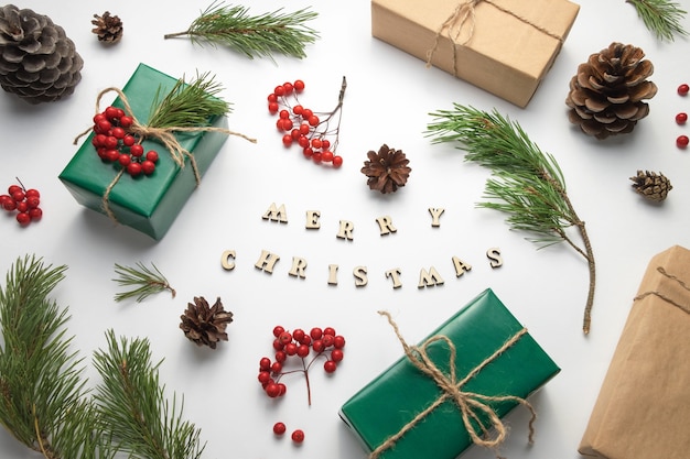 Weihnachtsgeschenke. Auf dem Tisch stehen Tannenzweige, Zapfen und Ebereschenbüschel zum Dekorieren von Geschenken. Die Inschrift Frohe Weihnachten.