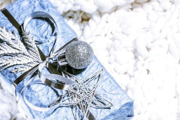 Weihnachtsgeschenke mit Geschenkbox in silberblauer Farbe, dekoriert mit Tannenzapfen und Zweigen auf weißem Hintergrund, Vorbereitung auf den Urlaub. Weihnachtsgeschenke und Neujahr. Handgefertigt. Selektiver Fokus.