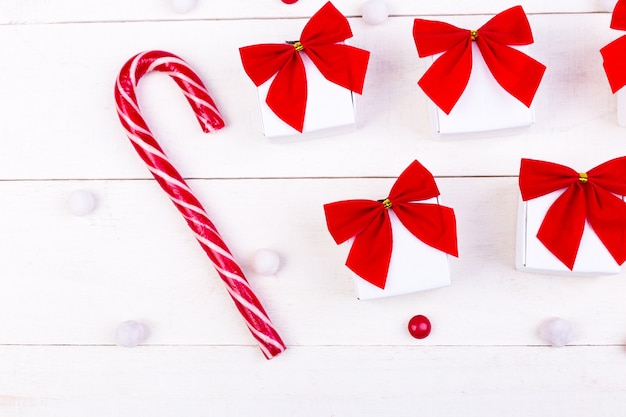 Weihnachtsgeschenke, weiße Kästchen mit roter Schleife und Bonbons auf weißem hölzernem Hintergrund