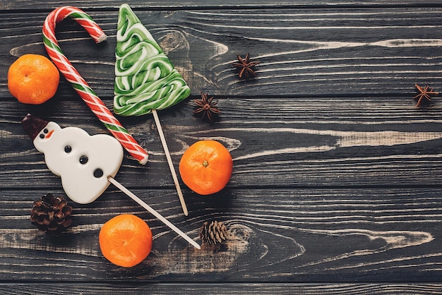 Weihnachtsgestreifte Süßigkeit und Baum- und Schneemannlutscher mit Mandarine und Anis auf rustikalem hölzernem Draufsichtweihnachtsgrußraum des Hintergrundes für Textwinterferien