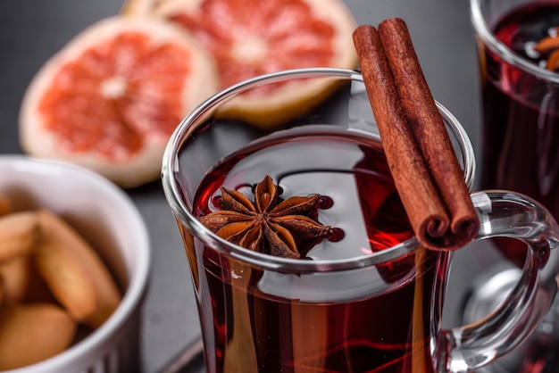 Weihnachtsglühwein mit Gewürzen und Früchten auf einem dunklen Tisch.