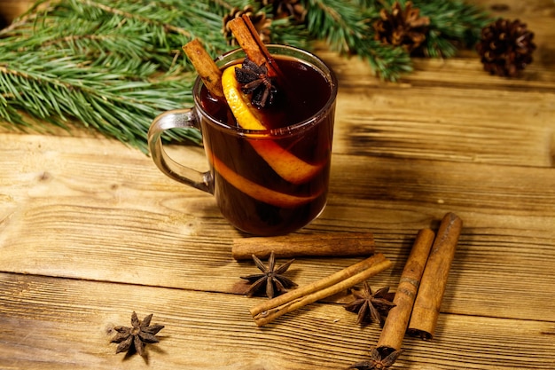 Weihnachtsglühwein mit Gewürzen und Tannenzweigen und Zapfen auf Holztisch