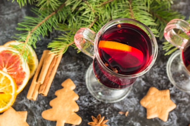 Weihnachtsglühwein mit Ingwerplätzchen Orangen-Zimt-Nelken-Anis und Tannenbaum auf dem schwarzen Tisch