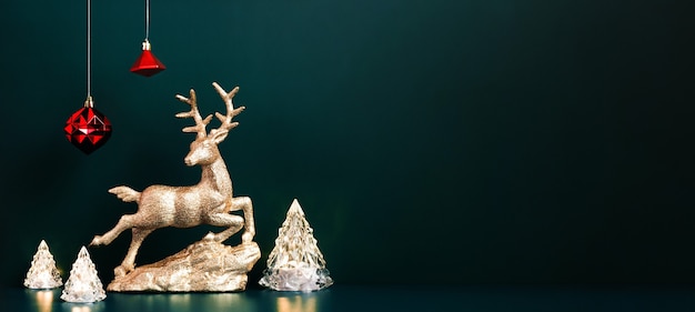 Weihnachtsgoldene Rentiere mit Weihnachtsbaumlampenlichtern mit roten Kugeln, die auf dunkelblauem, grünem Hintergrund hängen. Bannermodell für die Anzeige von Design oder Einladungskarte für Feiertagsveranstaltungen