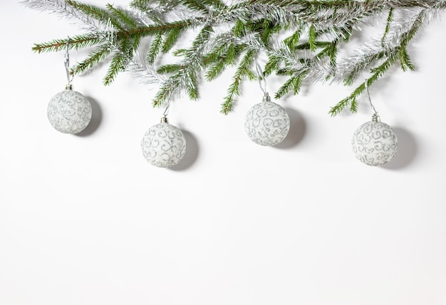 Weihnachtsgrenze aus natürlichen Fichtenzweigen, weiß mit silbernen Ornamentkugeln auf weißem Hintergrund.