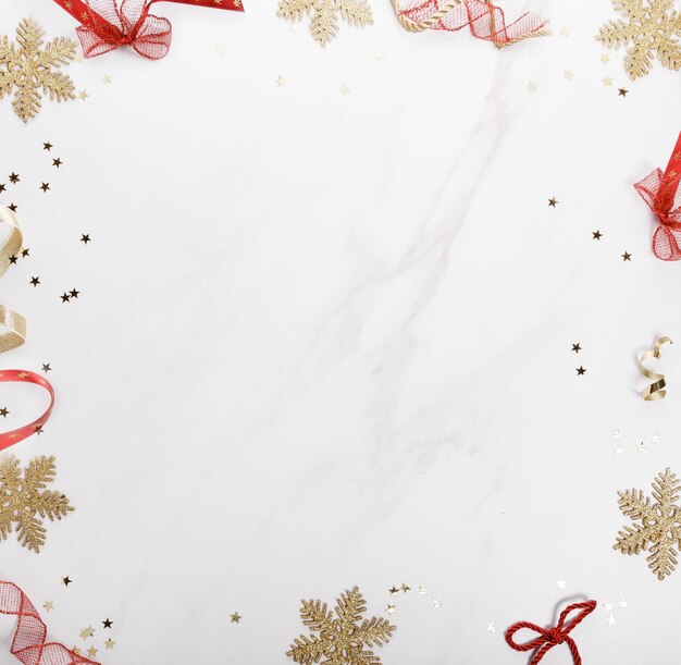 Weihnachtsgrenze aus roten Bogen und goldenen Schneeflocken von Weihnachtsdekorationen auf einem grauen Marmorgrund Flach gelegener Kopierraum