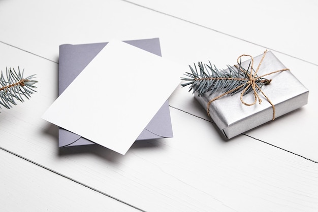 Weihnachtsgrüßkarten-Mockup mit grauem Umschlag, silberner Geschenkkiste und grünem Tannenbaumzweig