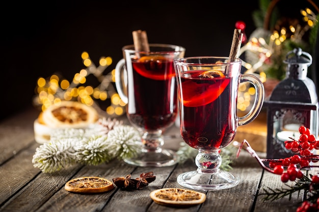 Weihnachtsheißer Glühwein mit Gewürzen und Früchten auf hölzernem Hintergrund mit Weihnachtsbeleuchtung