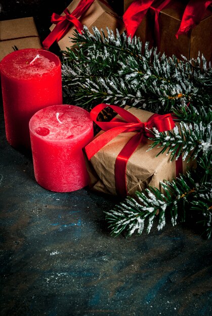 Weihnachtshintergrund für Grußkarte. Weihnachtsbaumaste mit Schneeeffekt mit festlichem rotem Band, Kiefernkegeln, Geschenkboxen und Kerzen, auf dunkelblauem Hintergrund