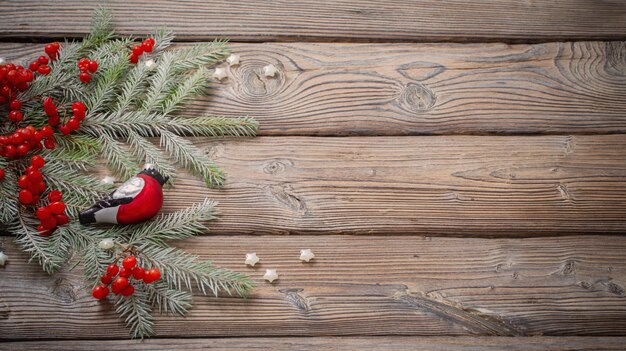 Weihnachtshintergrund mit roten Beeren Glasgimpel und Tannenzweigen auf dunklem Holztisch