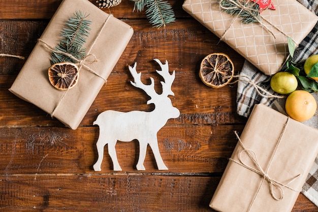 Weihnachtshintergrund mit weißem Spielzeughirsch, verpackten Geschenkboxen, Clementinen und Dekorationen auf Tisch