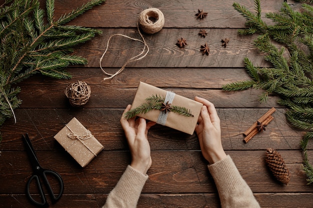 Weihnachtshintergrund von oben mit unerkennbarer junger frau, die geschenke an holztischkopie einwickelt...