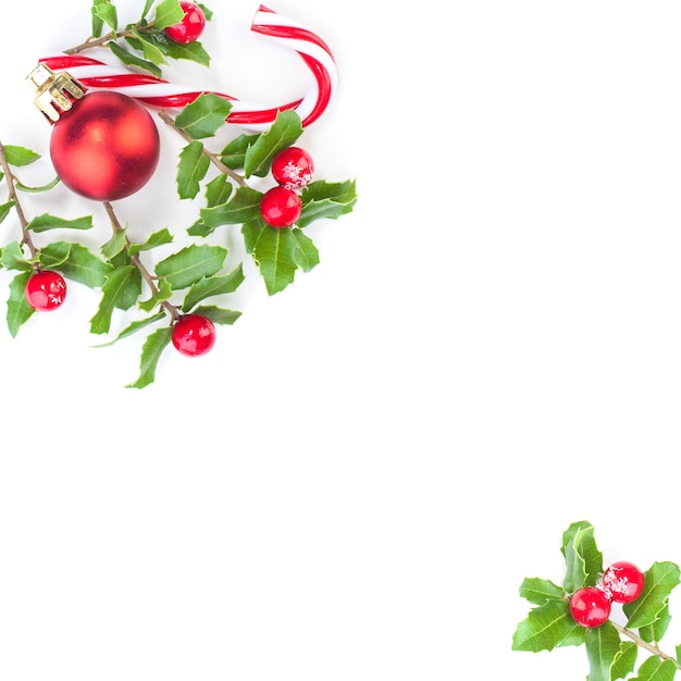 Foto weihnachtshintergrundgrenze mit stechpalmenbeeren, roten kugeln und süßigkeiten auf weiß