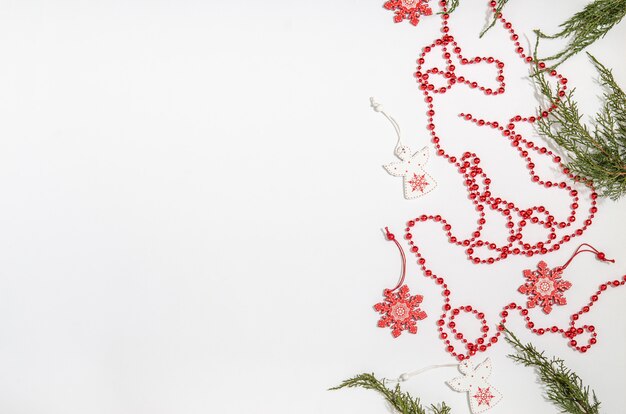 Weihnachtshölzerne Spielwaren in Form eines weißen Engels und einer roten Schneeflocke mit Wacholderbuschniederlassungen und roten Perlen mit Raum für Kopienraum mit einer Ebenenlage auf einem weißen Hintergrund.