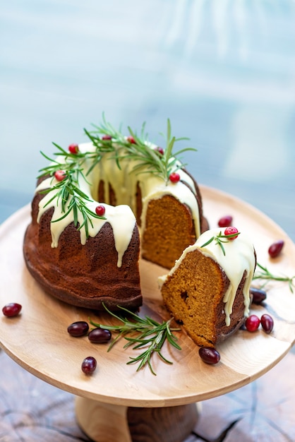 Weihnachtskaramellkuchen, Cutaway, dekoriert mit weißer Schokolade, Preiselbeeren und Rosmarin auf einem Holzständer. Festliche Backwaren. Weicher selektiver Fokus. Vertikal