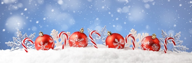 Weihnachtskarte mit dekorativen Kugeln, Süßigkeiten und Schneeflocken auf Schnee