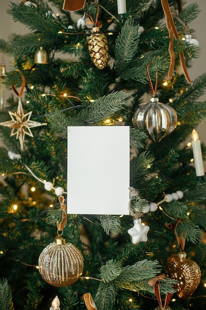 Foto weihnachtskarten-attrappe leere grußkarte auf dem hintergrund eines stilvoll geschmückten weihnachtsbaums mit goldenen lichtern platz für text vorlage für weihnachtsgrüße postkarte und vintage-ornamente