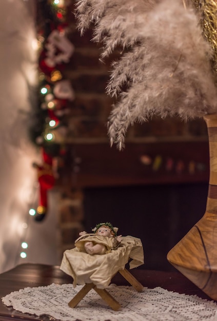 Weihnachtskarten Baby Jesus Vintage Figur in seiner Krippe mit Weihnachtsbeleuchtung und Kamin im Hintergrund