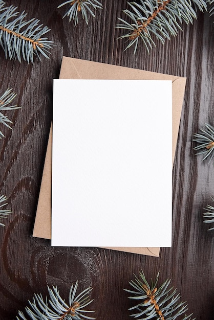 Weihnachtskartenmodell mit Umschlag und grünen Tannenzweigen auf braunem hölzernem Hintergrund Draufsicht flach gelegt