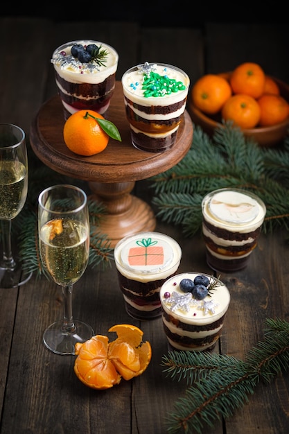 Weihnachtskleinigkeiten auf dem festlich gedeckten Tisch. Champagner, Mandarinen und Neujahrsdessert aus Keks-, Sahne- und Beerenfüllung.
