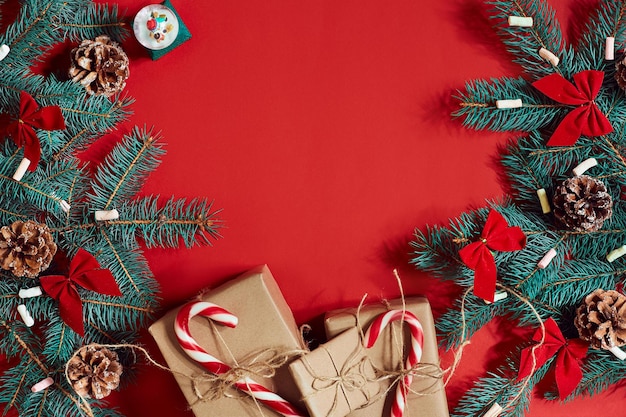 Weihnachtskomposition aus Tannenzapfen, Fichtenzweigen und Stapel Geschenkboxen auf rotem Hintergrund. Ansicht von oben. Platz kopieren. Stillleben. Flach liegen