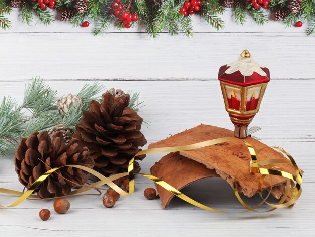 Weihnachtskomposition aus Tannenzapfen, Laterne, Haselnüssen, Baumrinde und Kiefernzweig auf heller Holzoberfläche und Hintergrund mit Tannenrand