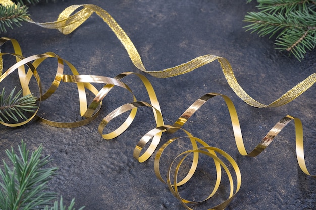 Foto weihnachtskomposition aus tannenzweigen und einem goldband auf schwarzem öl mit goldprägungshintergrund.