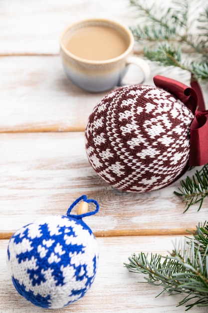 Weihnachtskomposition. Dekorationen, gestrickte Bälle, Tannen- und Fichtenzweige, Tasse Kaffee auf weißem Holztisch.