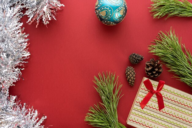 Weihnachtskomposition. Eine Schachtel mit einem Geschenk und Fichtenzweigen auf rotem Grund. Fichtenzapfen und Weihnachtsschmuck. Flache Lage, Draufsicht, Platz für Text
